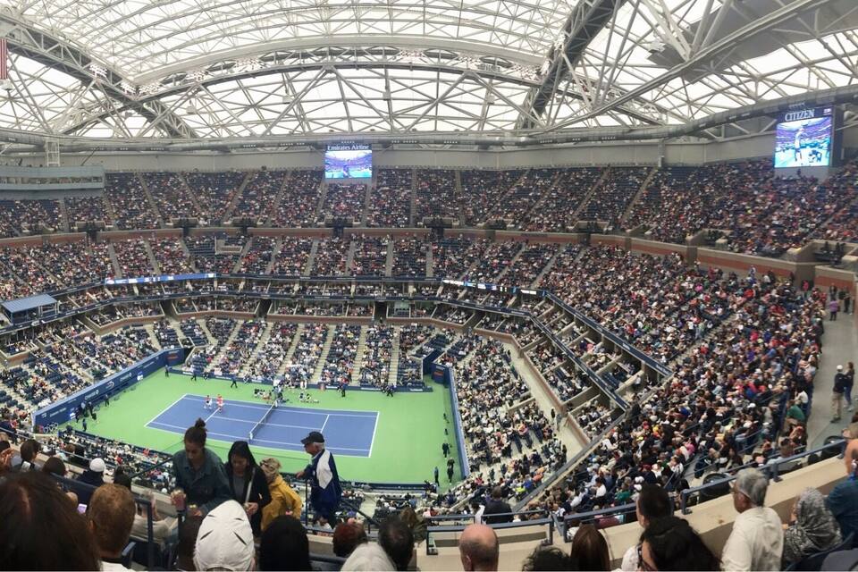 Un estadio interior amplio con cancha de tenis, múltiples pantallas y una multitud de espectadores.