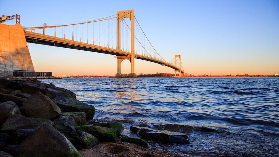 A large suspension bridge over a body of water with rocky shoreline in the foreground.