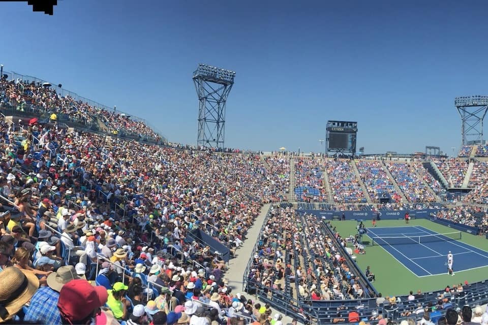 Un estadio grande lleno de espectadores, una cancha de tenis y dos torres de iluminación altas.