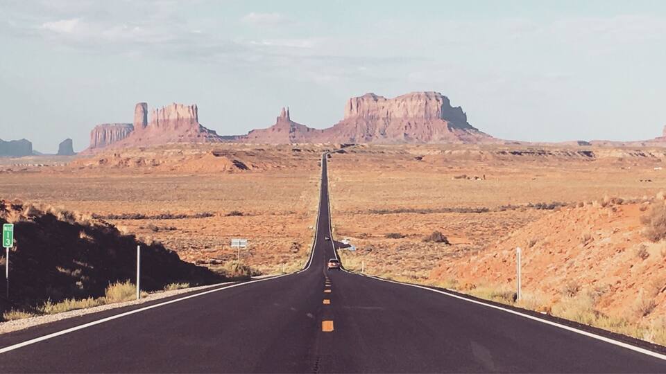 A straight road leading towards rock formations in a desert landscape.
