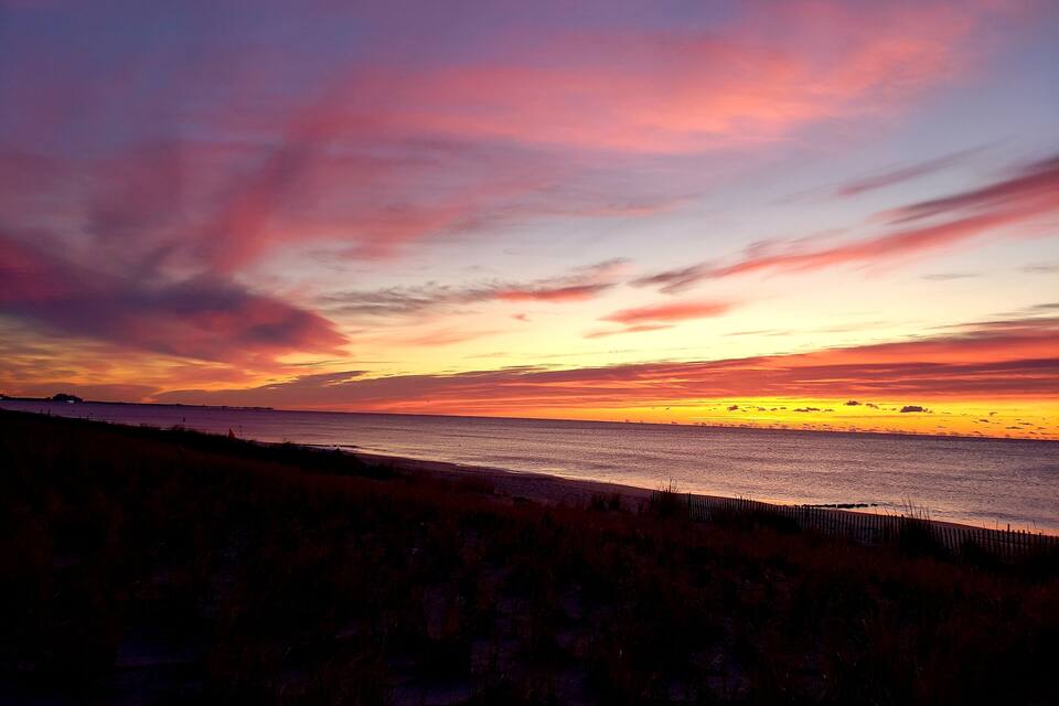 Atardecer sobre una playa con una valla en primer plano.