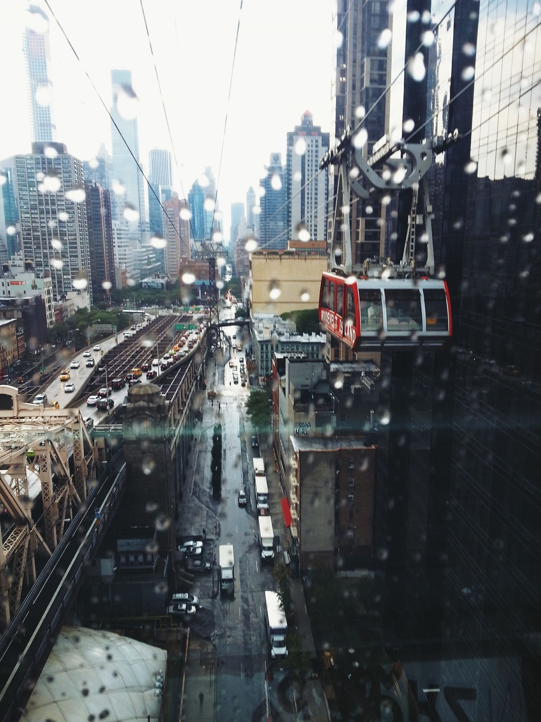 Paisagem urbana com um teleférico vermelho, uma ponte e edifícios altos.