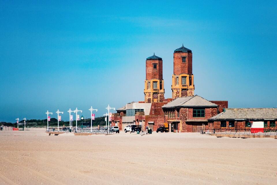 Un edificio grande de ladrillo con dos torres destacadas y un primer plano arenoso.