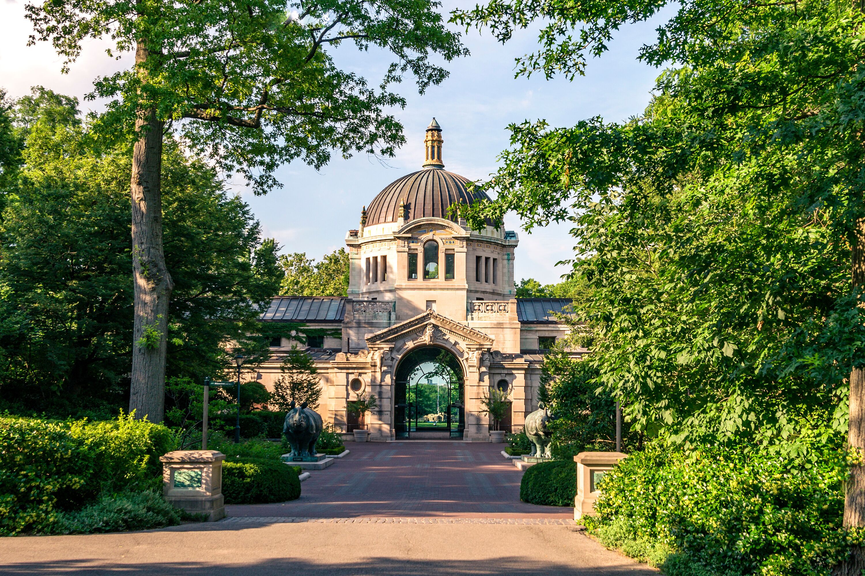 Un bâtiment historique surmonté d’un dôme, entouré d’une végétation luxuriante et accessible par un chemin pavé menant à son entrée.