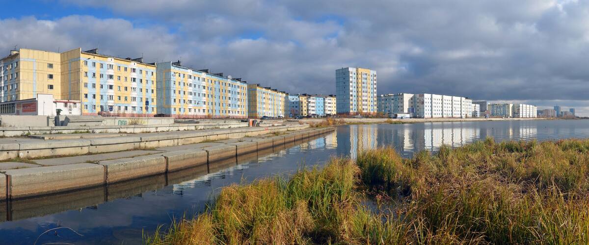 A waterfront with multi-story residential buildings and a calm body of water reflecting the structures.