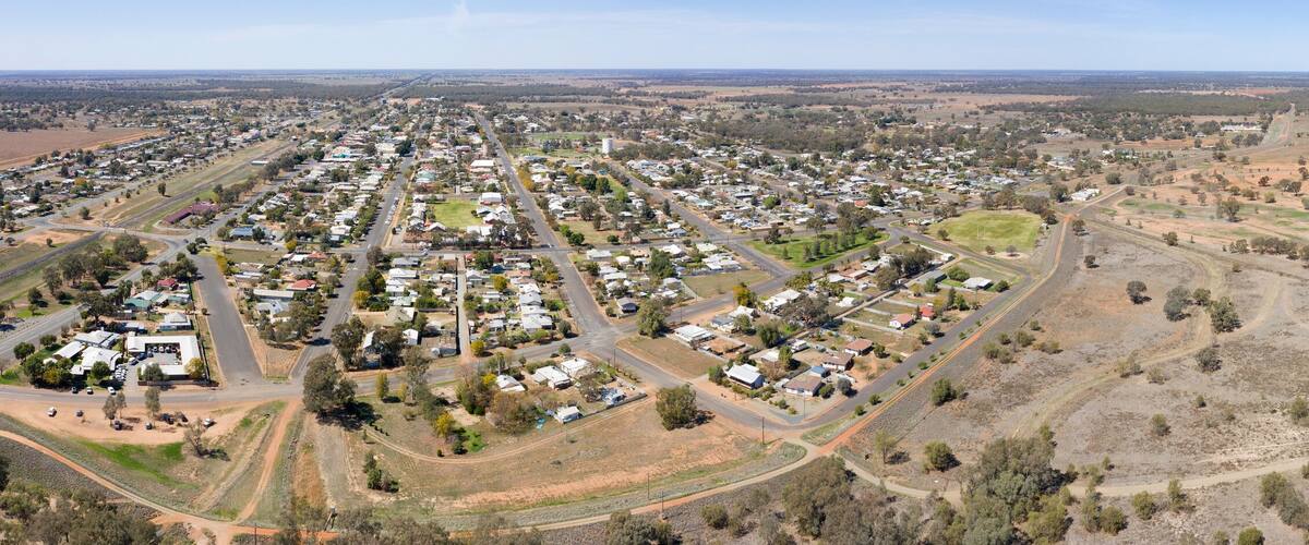 An aerial view of a town with a river running through it, surrounded by open fields and sparse vegetation.