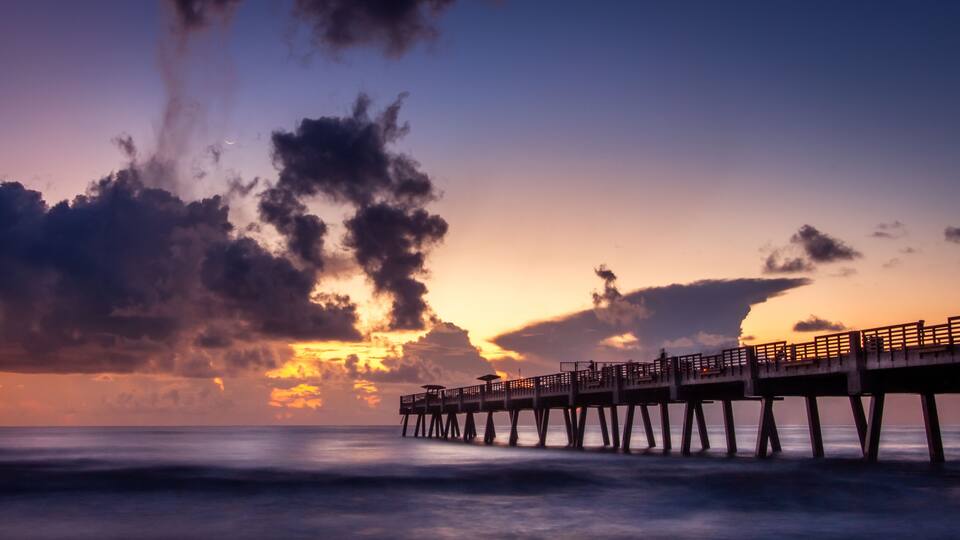 A pier extending into the ocean at sunset with clouds in the sky.