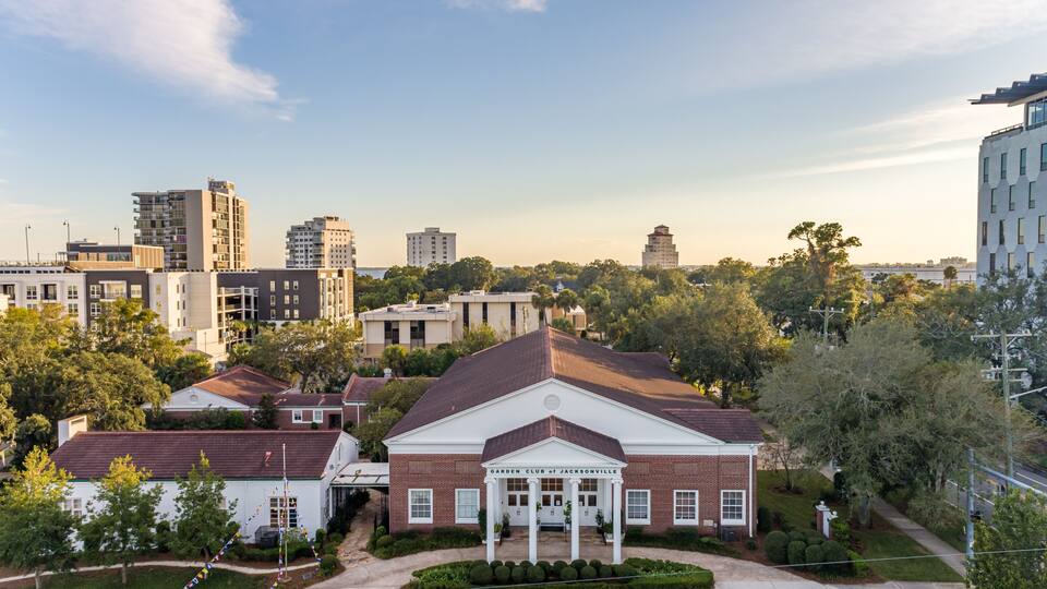A historic building with a central portico, surrounded by modern residential buildings and a clear sky.