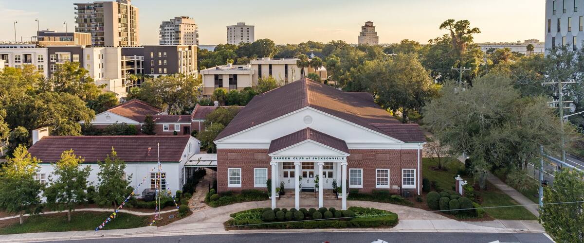 A historic building with a central portico, surrounded by modern residential buildings and a clear sky.