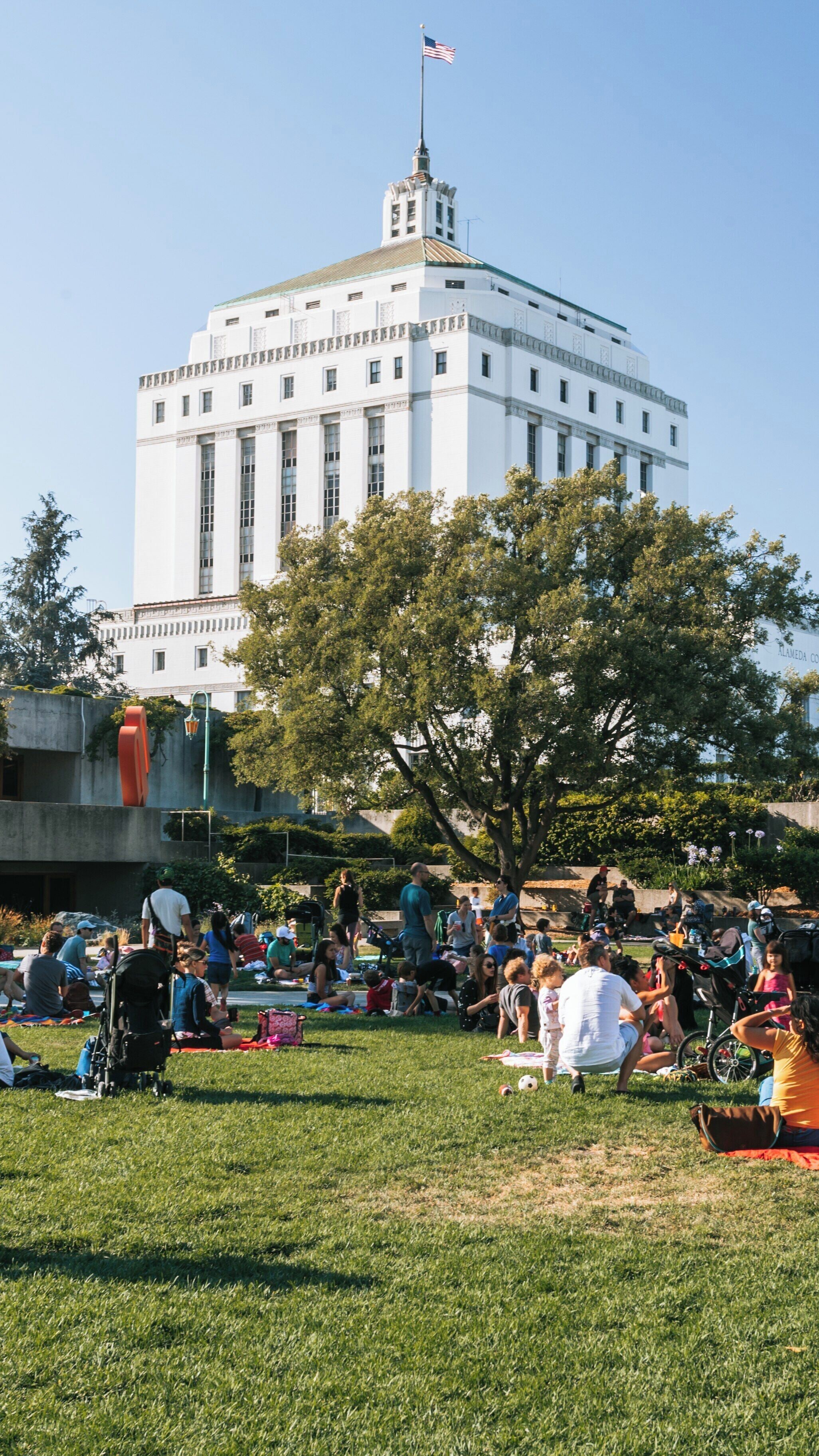 Visitors enjoy a sunny day at Oakland Museum of California with views of Chinatown and people relaxing on the grass