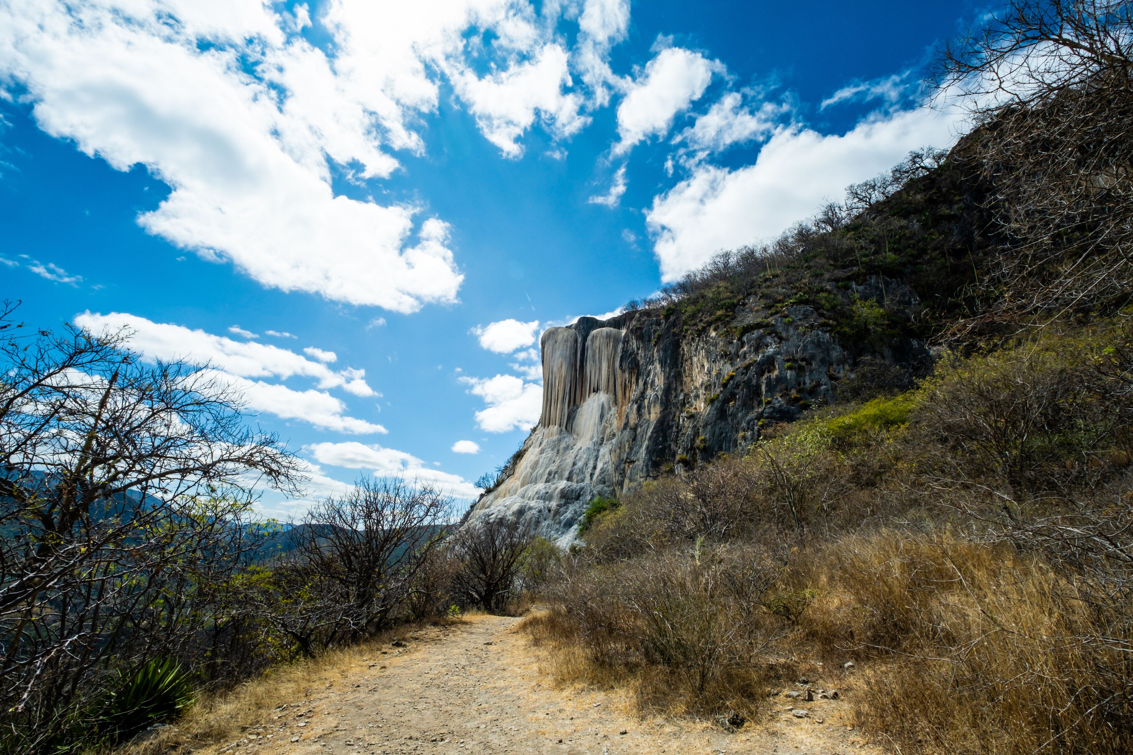 A dirt path leading to a large rock formation with a waterfall.