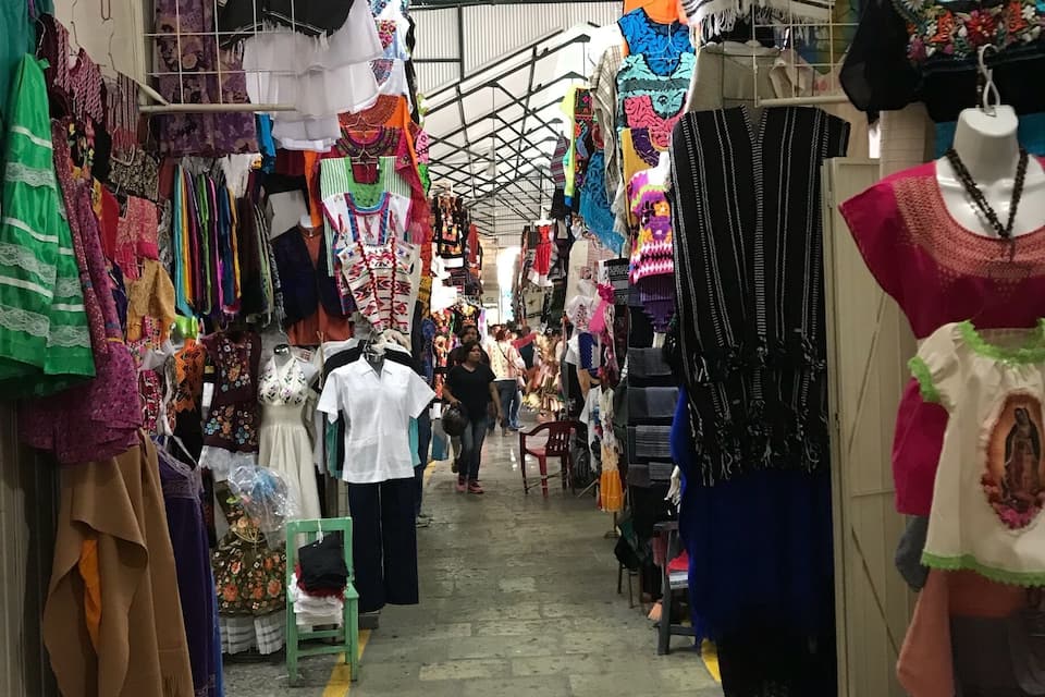 Un mercado con coloridos textiles y prendas de vestir exhibidas en estantes y maniquíes.
