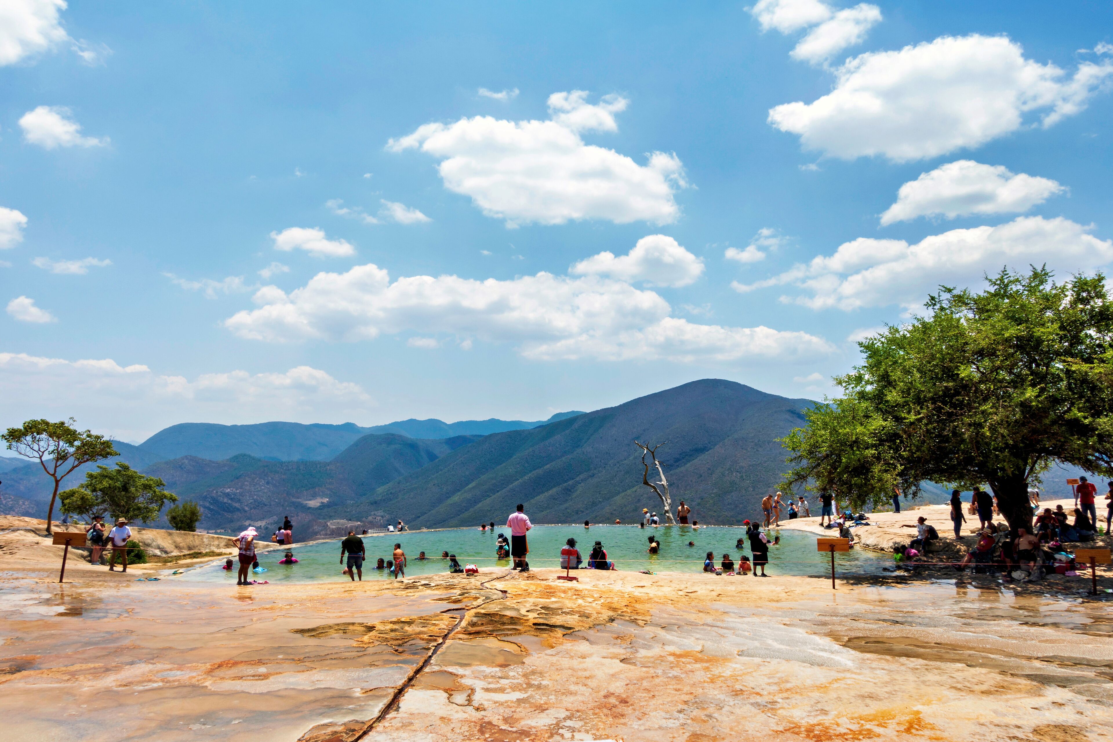 A geothermal pool with people swimming and relaxing, surrounded by mountains and trees.
