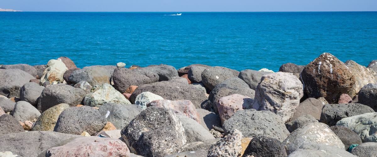 A rocky shoreline with a clear blue sea and a distant boat.