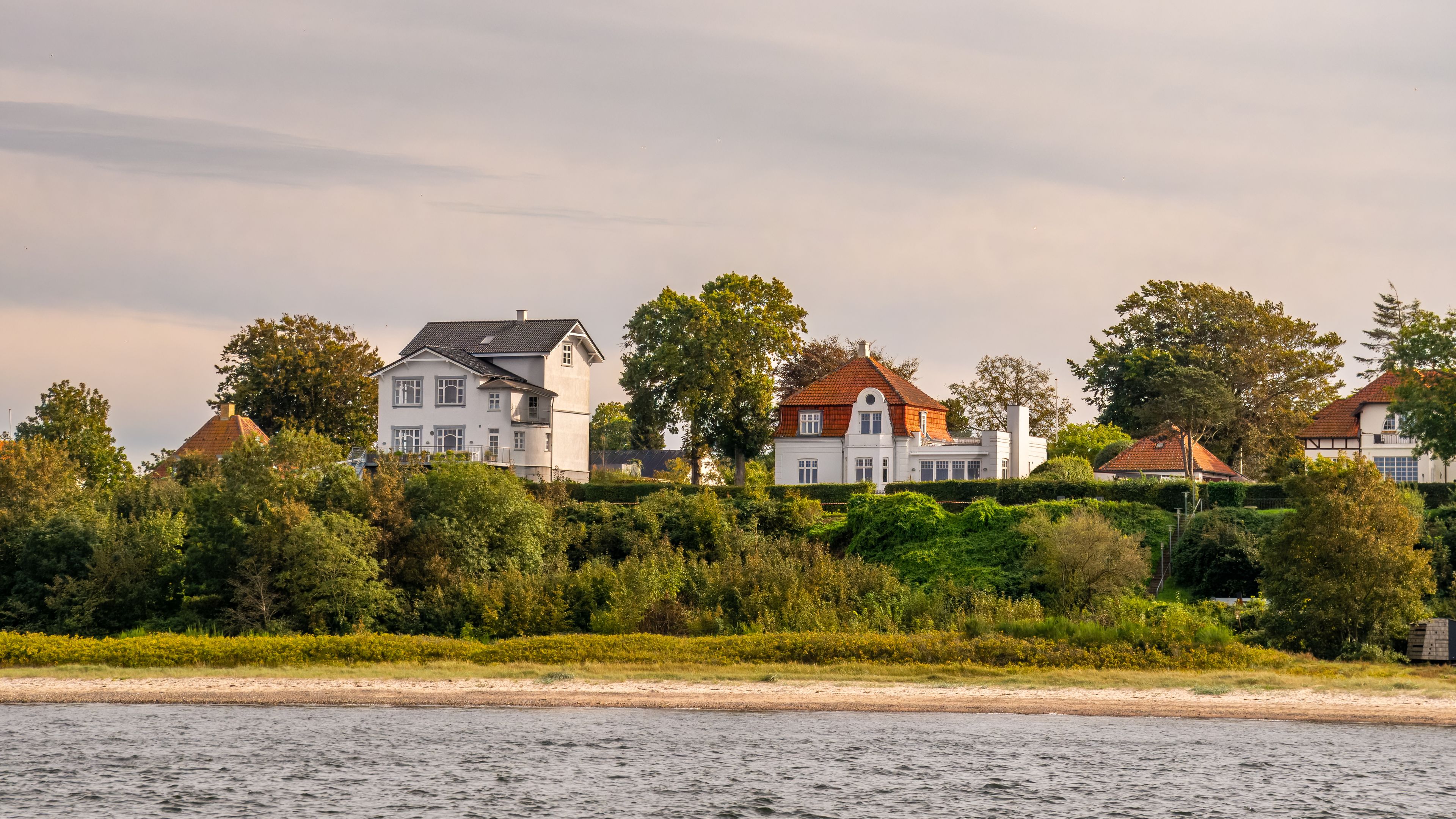 A waterfront with houses, trees, and a sandy beach.