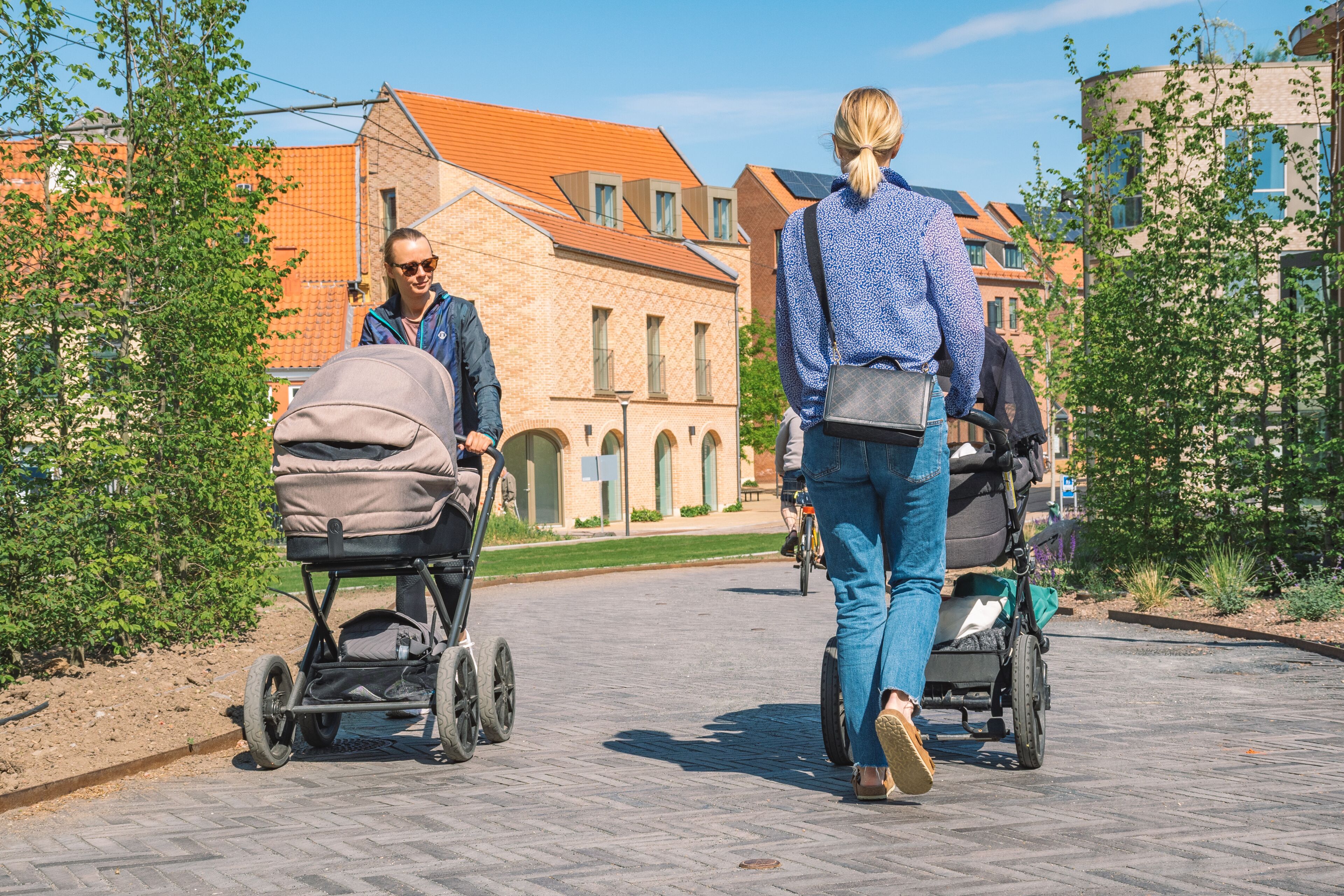 Beautiful young blonde hair girls with stroller walking on a new bike path or road between modern buildings in the center of Odense, Denmark