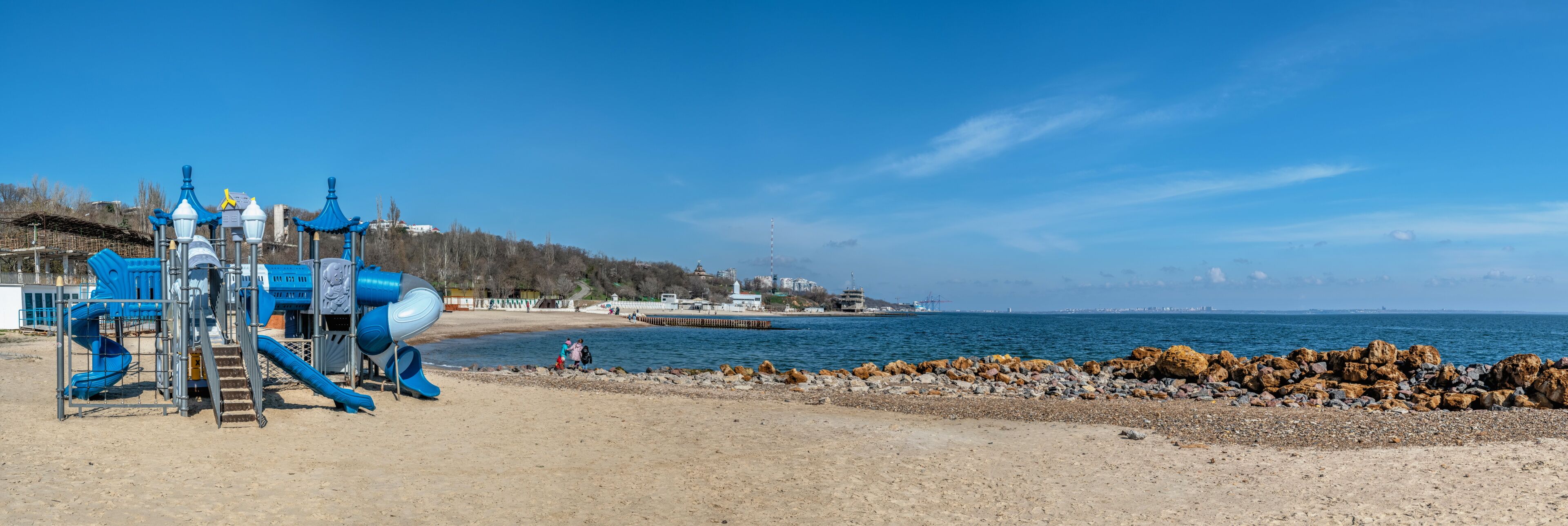 A playground with slides and a sandy beach with rocks.