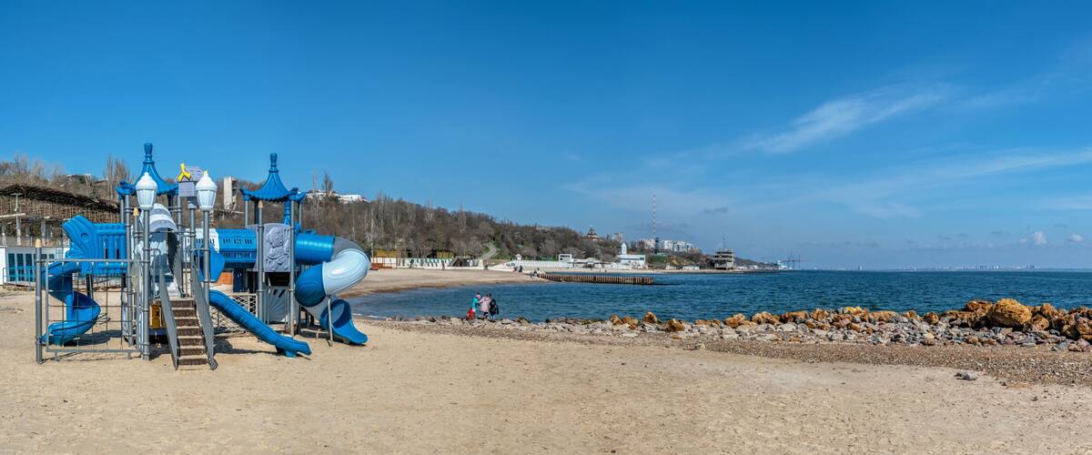 A playground with slides and a sandy beach with rocks.