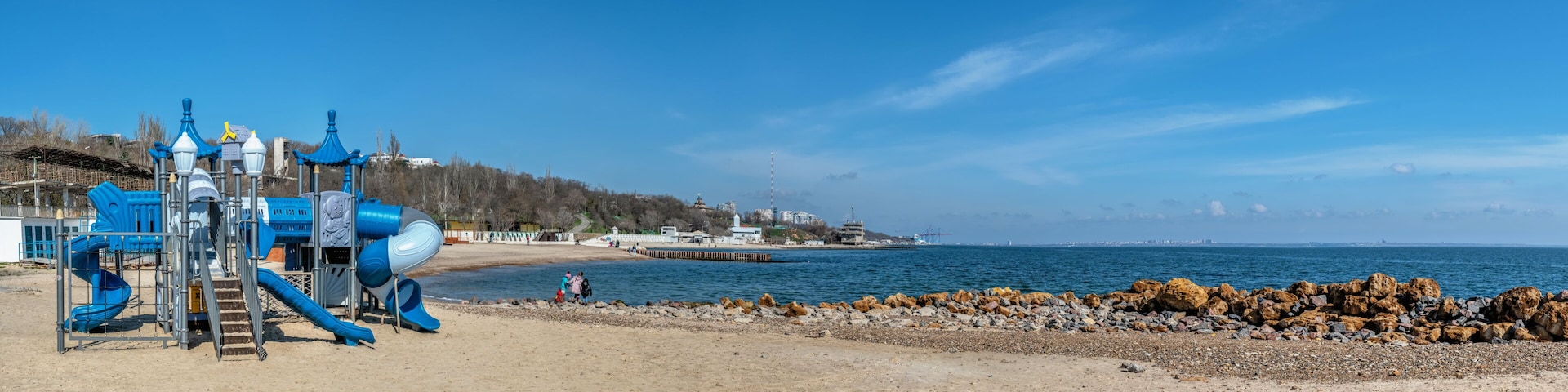 A playground with slides and a sandy beach with rocks.