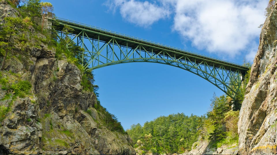 A green metal bridge spanning a river between rocky cliffs.