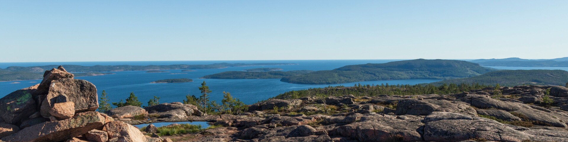 Paisagem rochosa com vista ampla para um lago e montanhas ao longe.