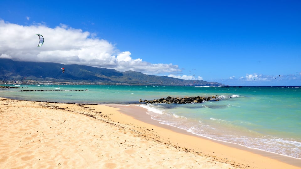 A beach with clear turquoise water, a sandy shore, and a mountainous backdrop.