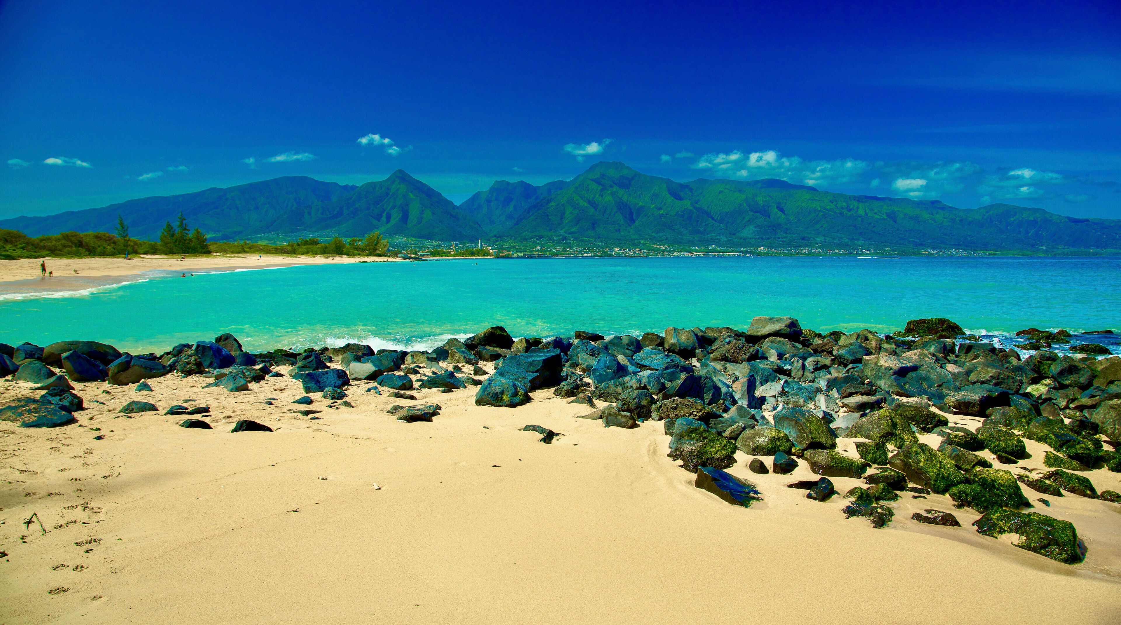 A serene beach with turquoise waters and distant green mountains under a clear blue sky. Kanaha beach park, West Maui Mountains, Kite beach, Kahului, Hawaii