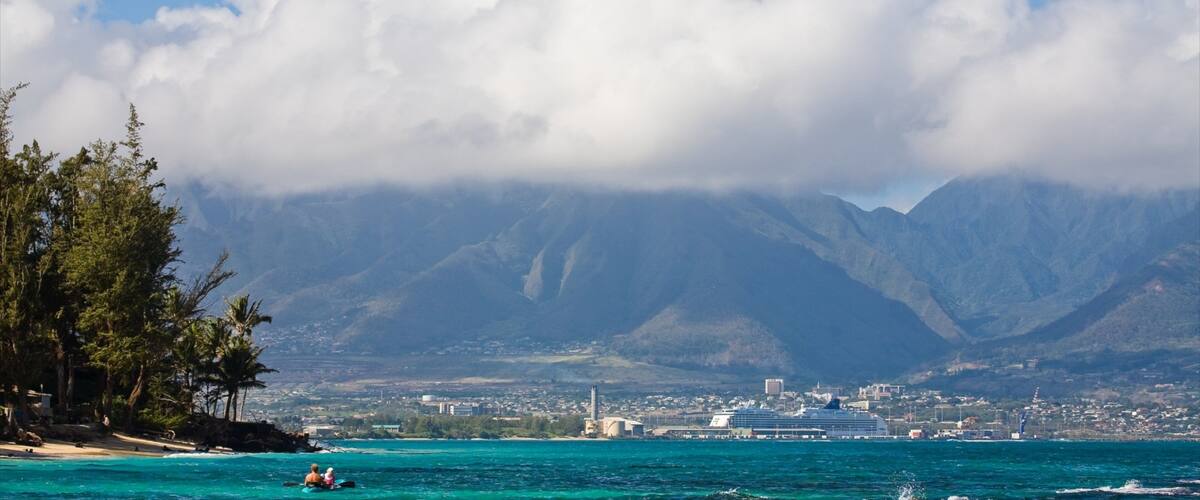 A coastal city with a cruise ship docked, mountains in the background, and a clear sky with clouds.