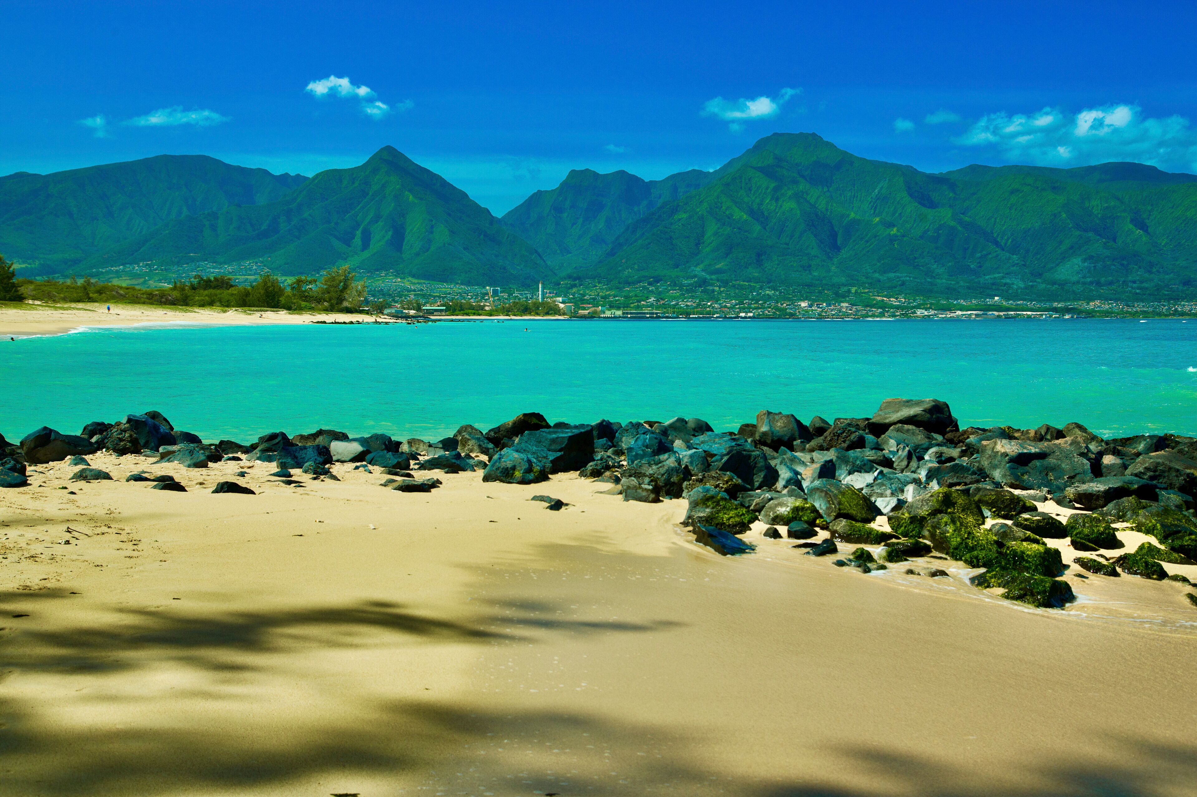 Tropical beach with turquoise waters, rocky shoreline, and lush mountains in the background. Kanaha beach park, West Maui Mountains, Kite beach, Kahului, Hawaii