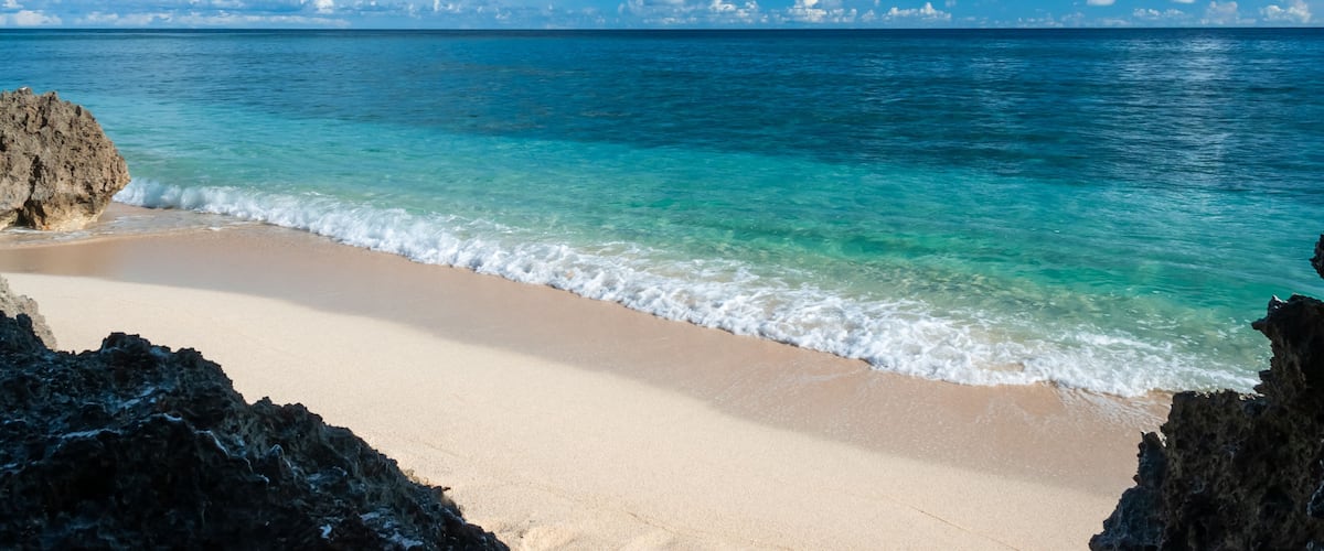 A beach with clear turquoise water, a sandy shore, and rocky outcrops.