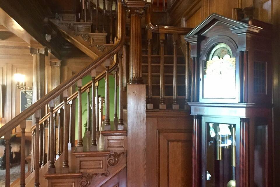 Una imponente escalera de madera con barandillas ornamentadas y un gran reloj de pie.