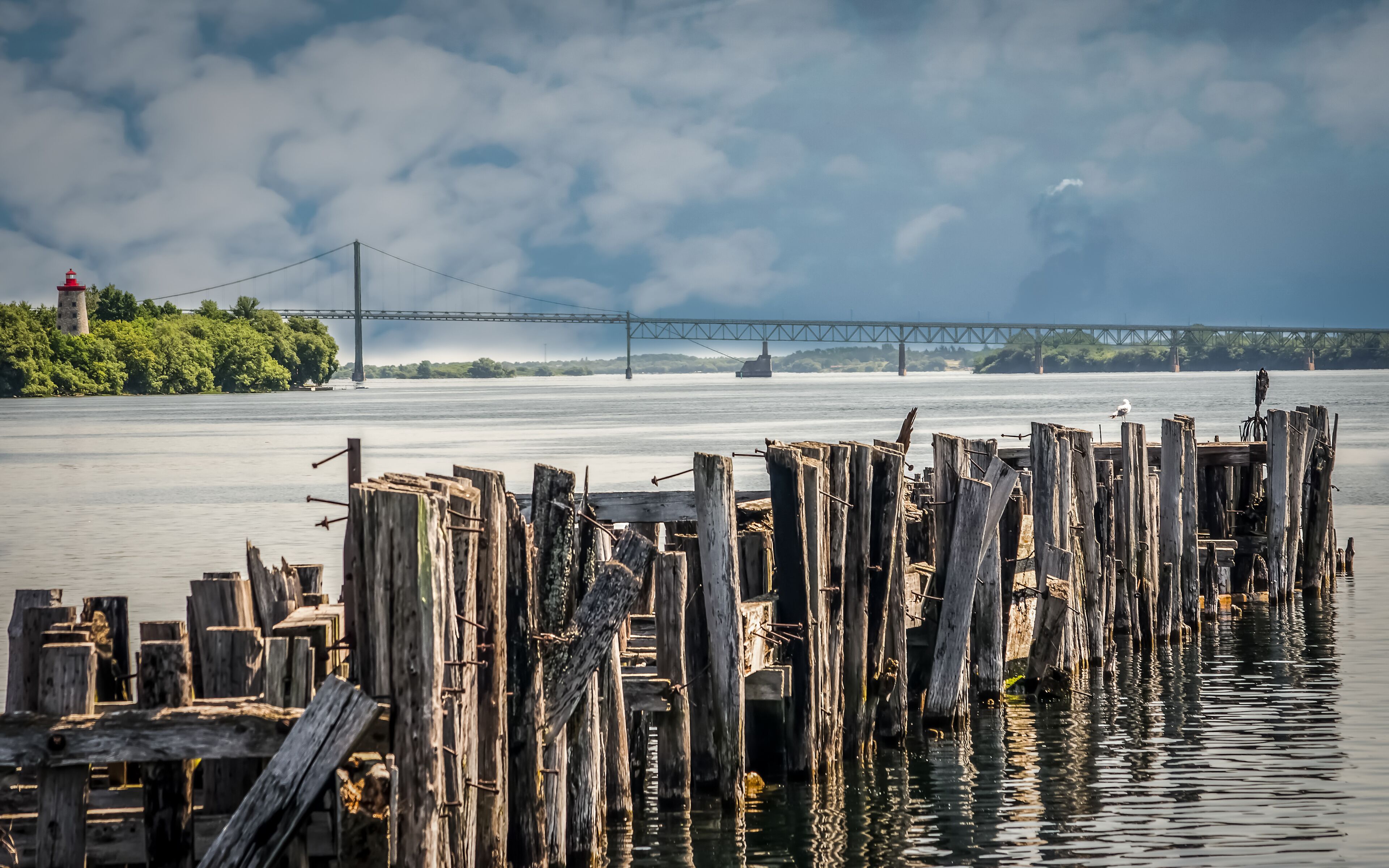 A wooden pier with a lighthouse in the background and a bridge across the water.