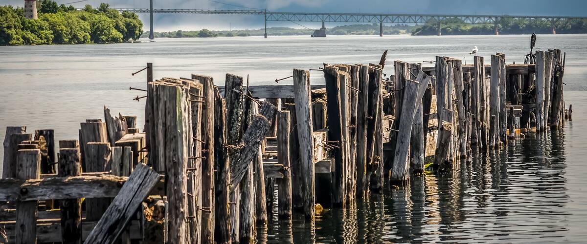 A wooden pier with a lighthouse in the background and a bridge across the water.