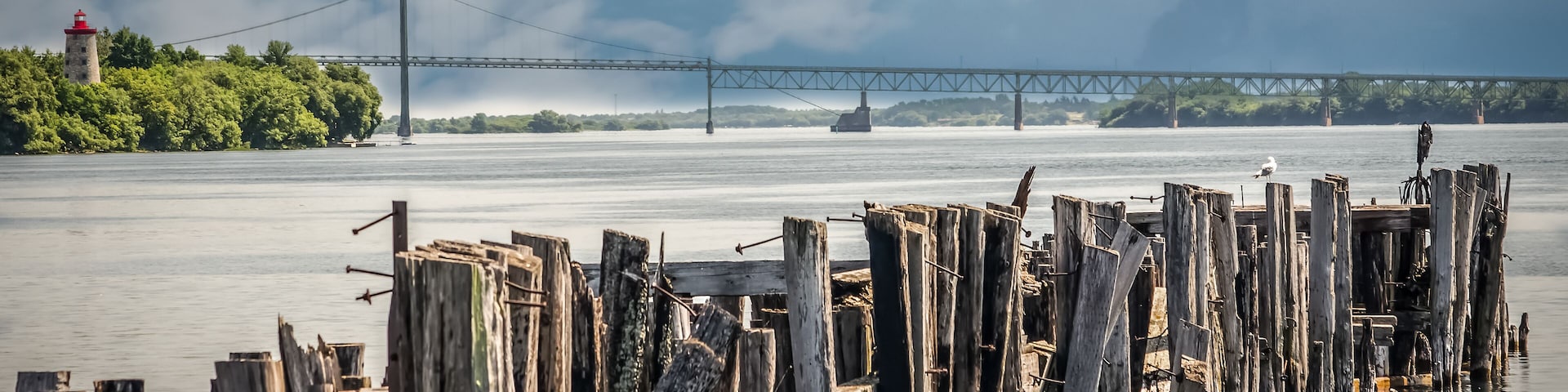 A wooden pier with a lighthouse in the background and a bridge across the water.