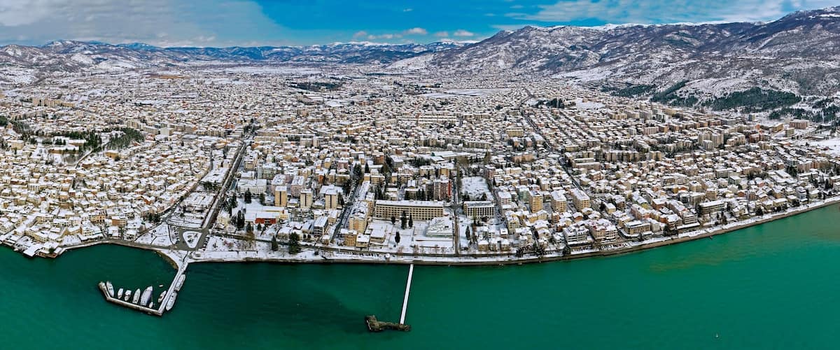 En vy över en kuststad från ovan, med snötäckta byggnader och berg i bakgrunden.