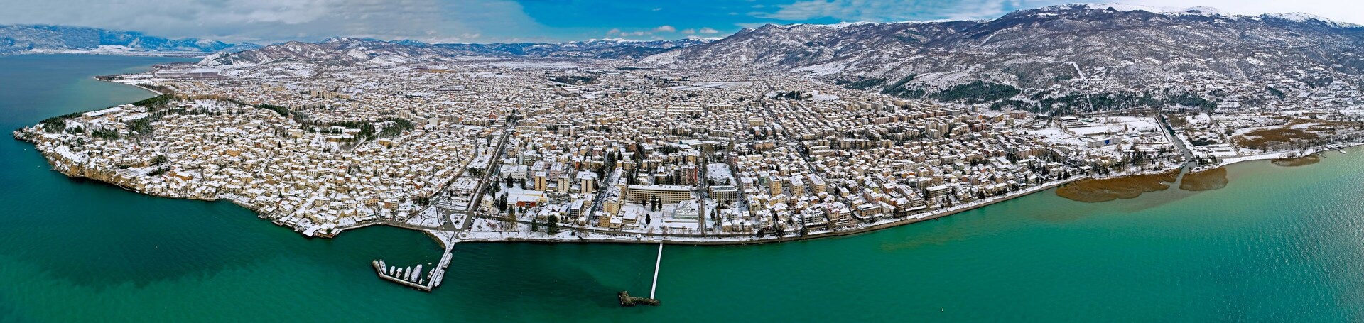 Vista aérea de una ciudad costera con edificios nevados y montañas al fondo.