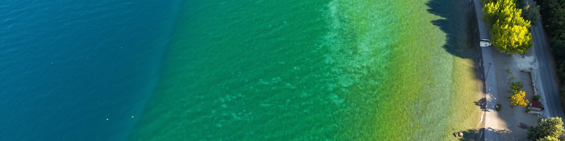 A coastal area with clear turquoise waters, a sandy beach, and a road lined with trees.
