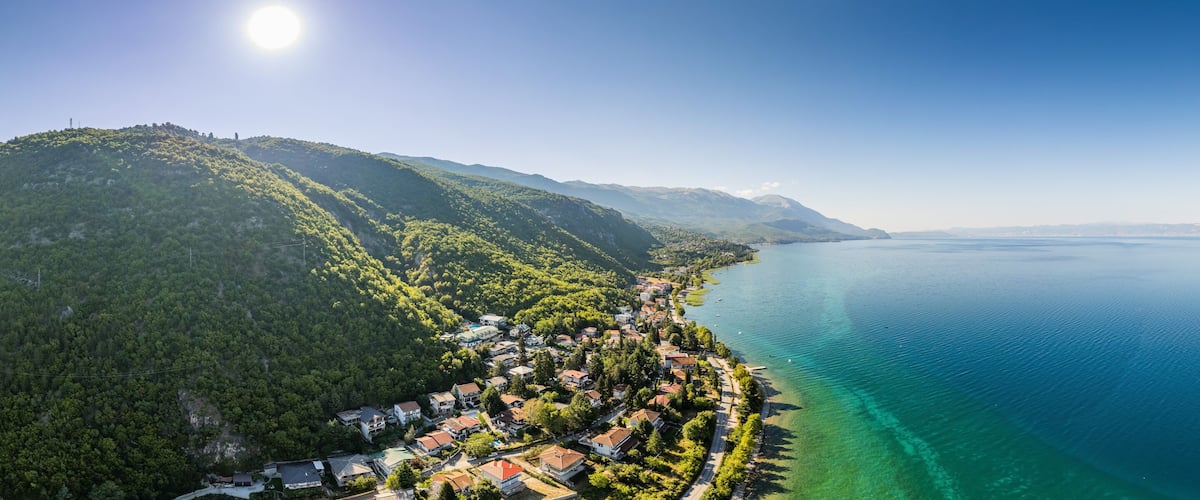 A coastal town nestled between lush green hills and a calm blue sea.