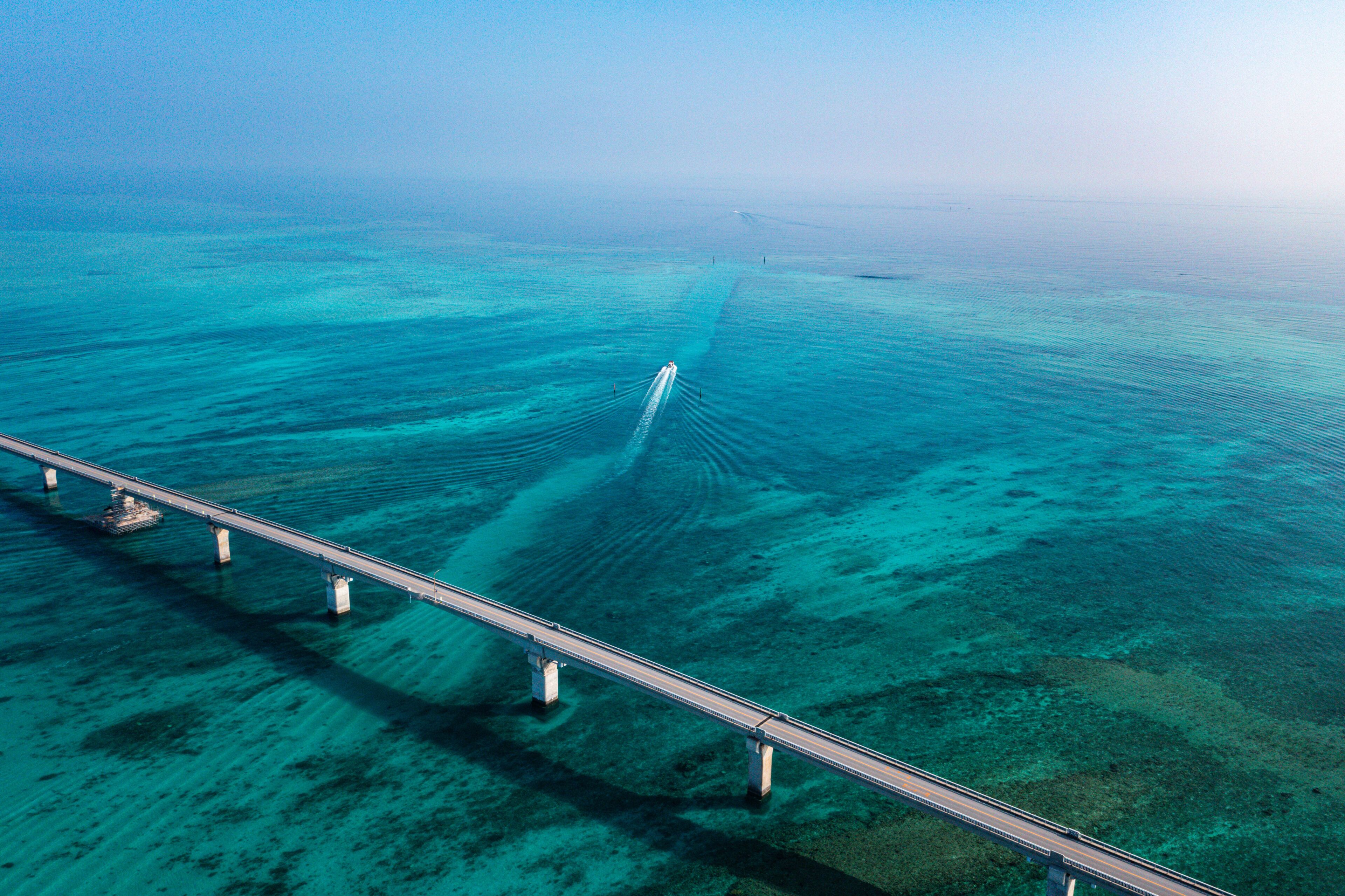 Een vogelperspectief van een brug boven een helderblauwe zee, met zichtbare onderwaterlandschappen.