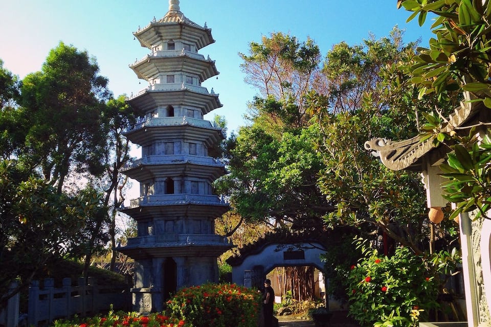 A multi-tiered pagoda surrounded by lush greenery and a stone bridge.
