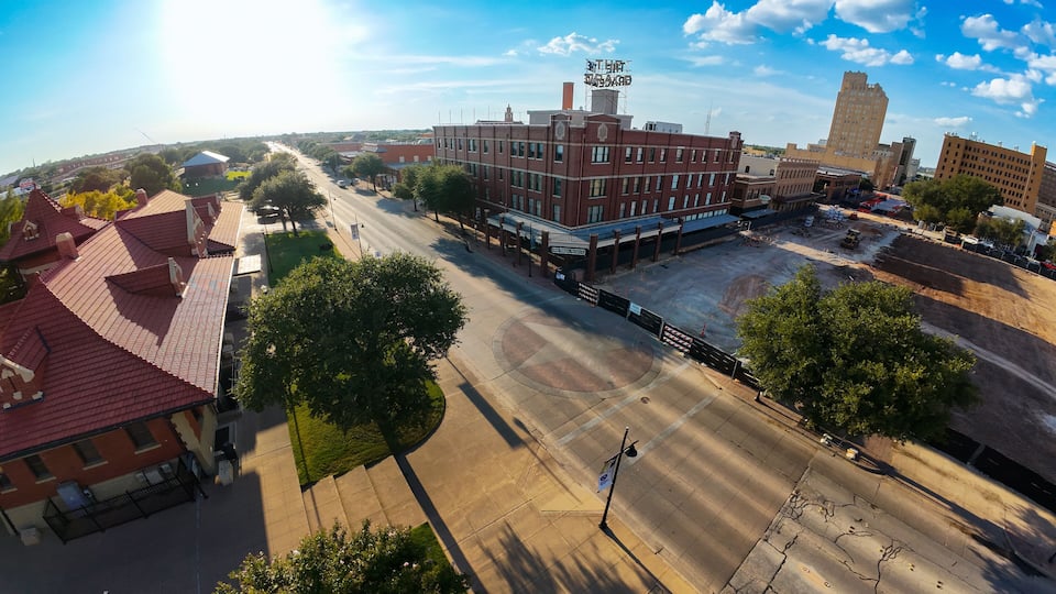 A street view with a large red brick building, a construction site, and a tall building in the background.