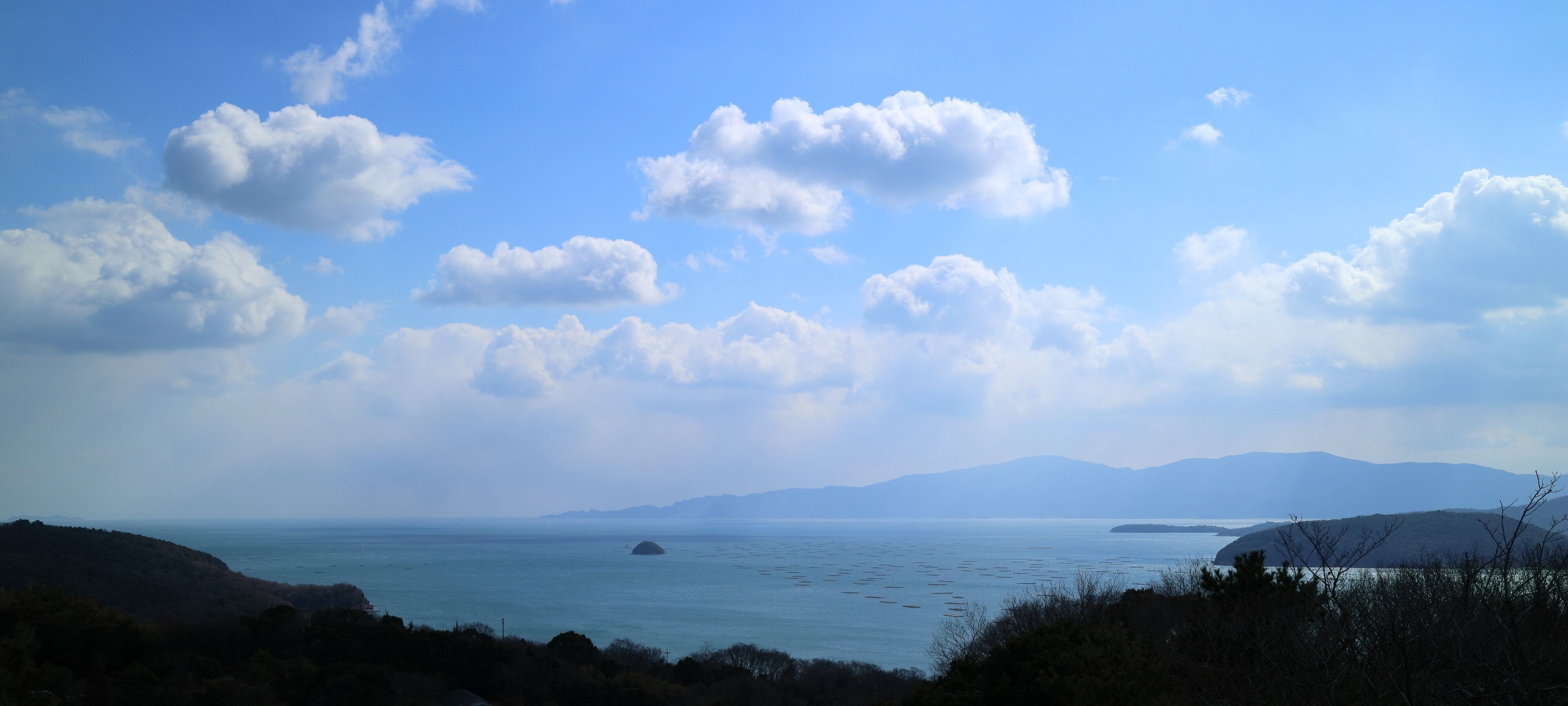 Un paisaje costero con cielo despejado, mar tranquilo y montañas a lo lejos.