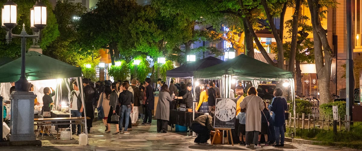 A nighttime outdoor market with people and stalls under green tents.