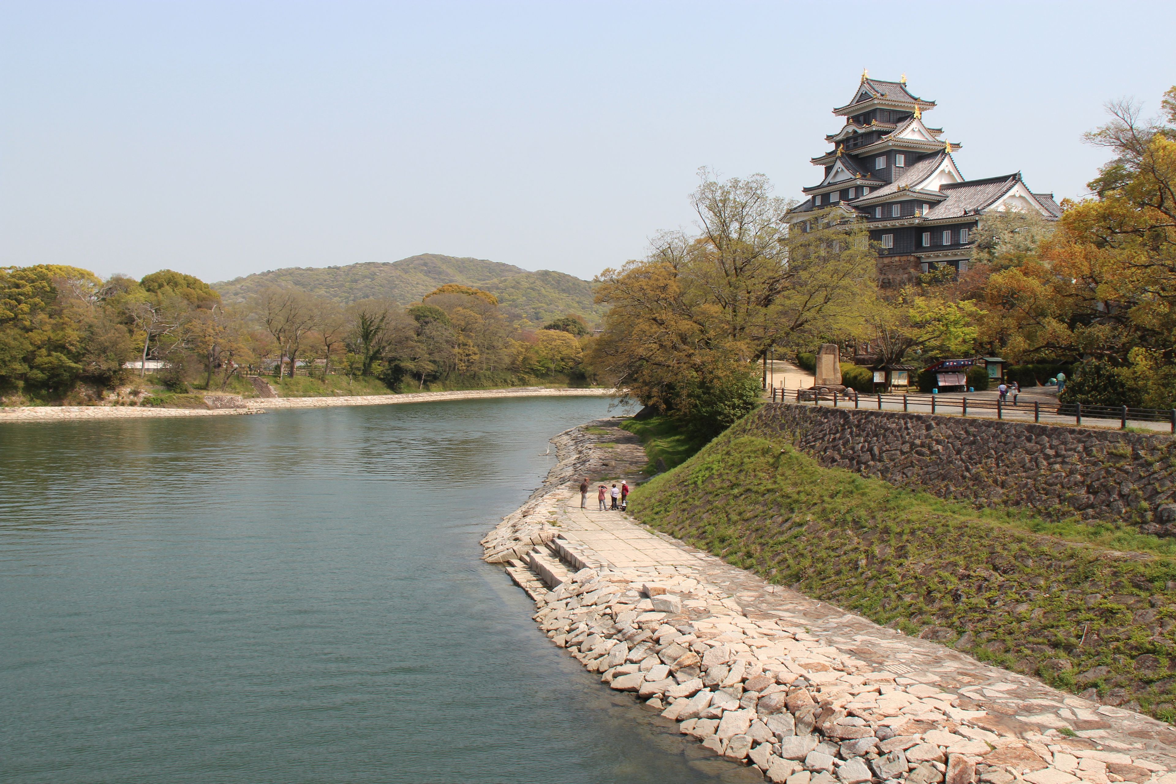 Un castillo japonés tradicional junto a un río, con escalones de piedra que bajan hasta el agua.