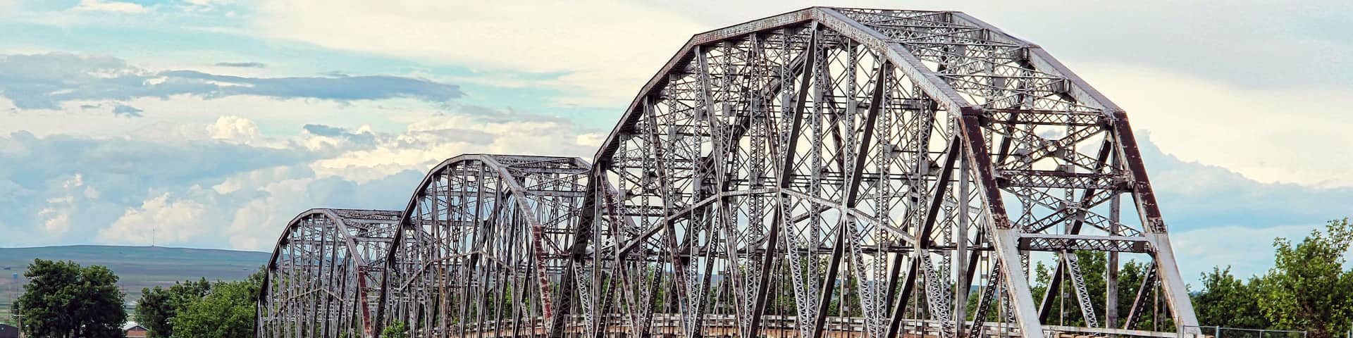 A large, rusted metal bridge with multiple arches spanning a highway.