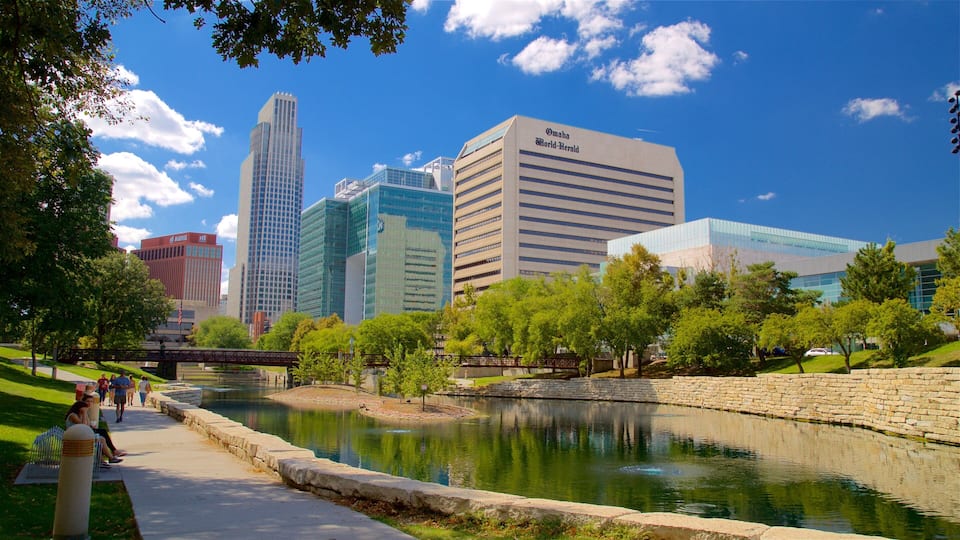 A cityscape with modern buildings, a river, and a park with people walking.