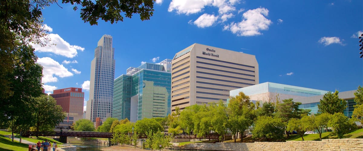 A cityscape with modern buildings, a river, and a park with people walking.