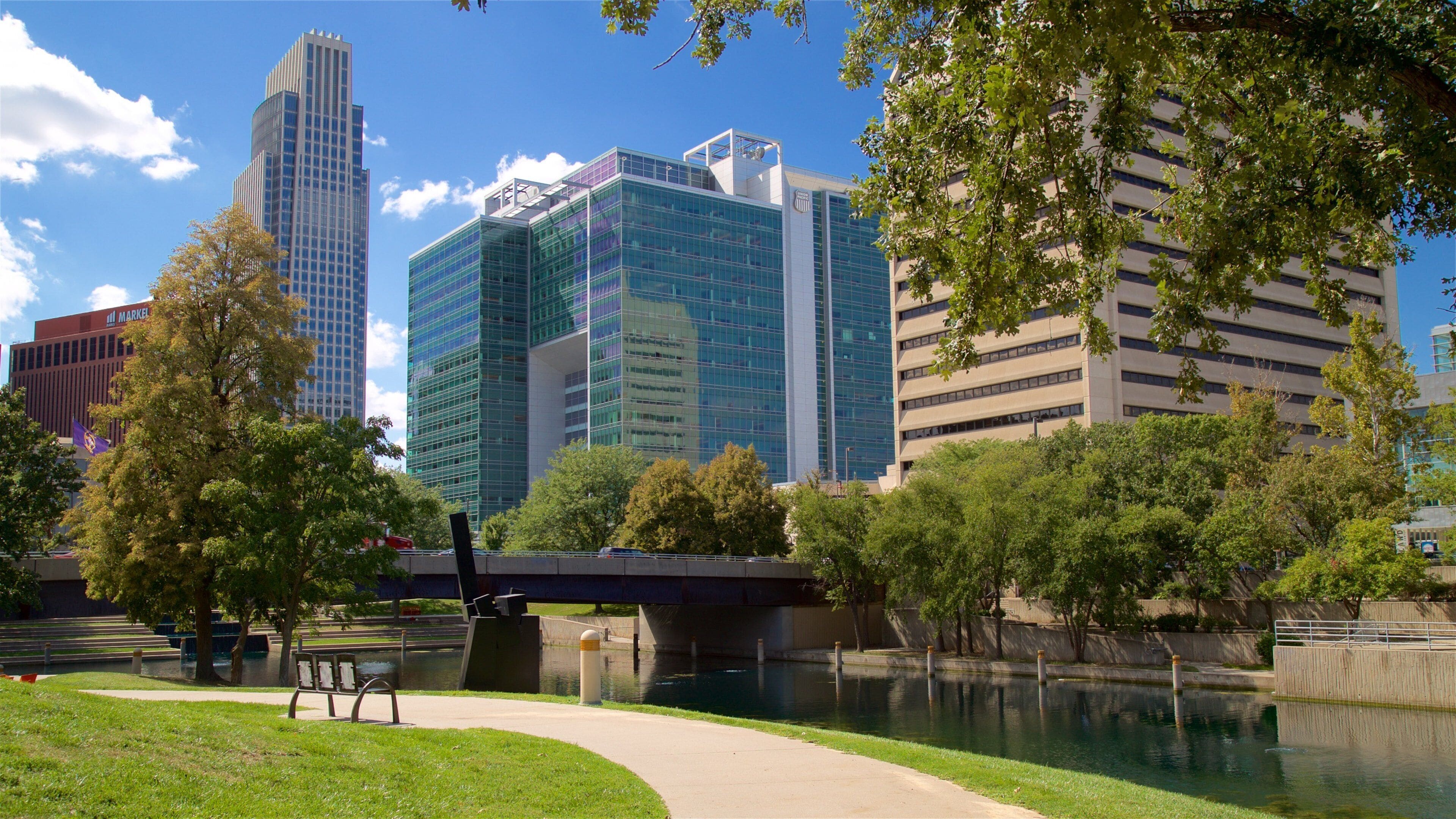 A river with a bridge, surrounded by trees and modern buildings.