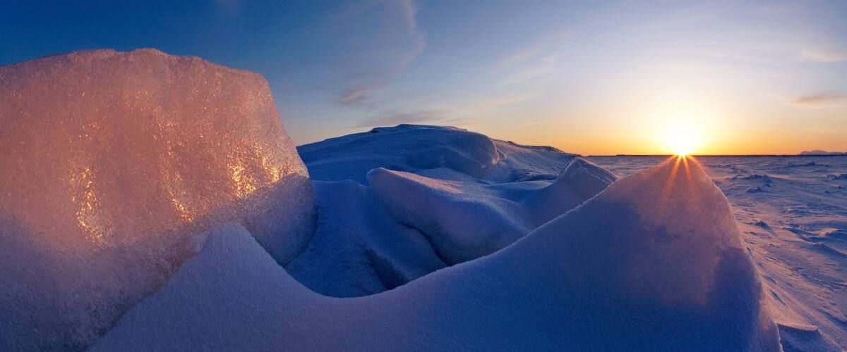 A snowy landscape with ice formations and the sun setting in the background.