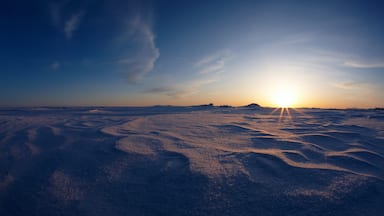 A snowy landscape with the sun setting in the background.